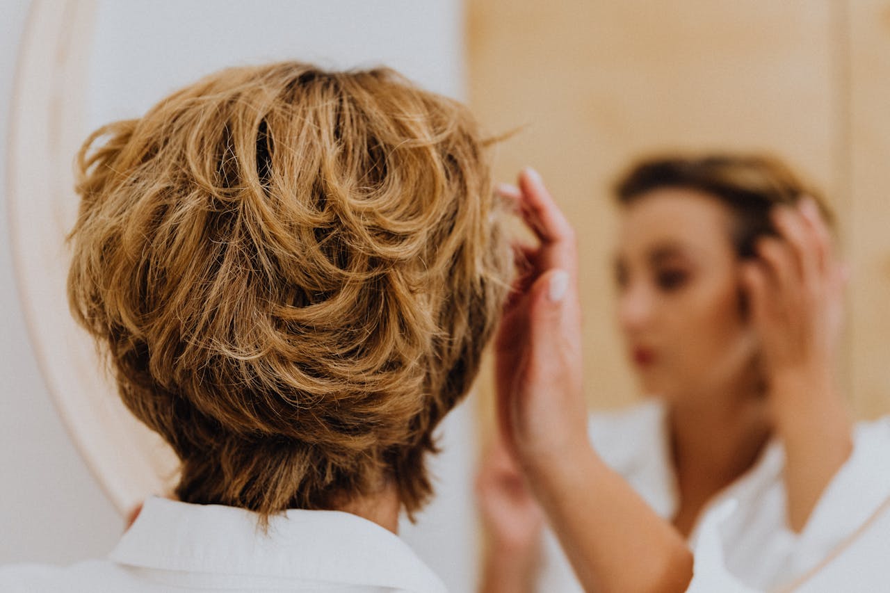 Back view of a woman styling her short hair while looking in the mirror.