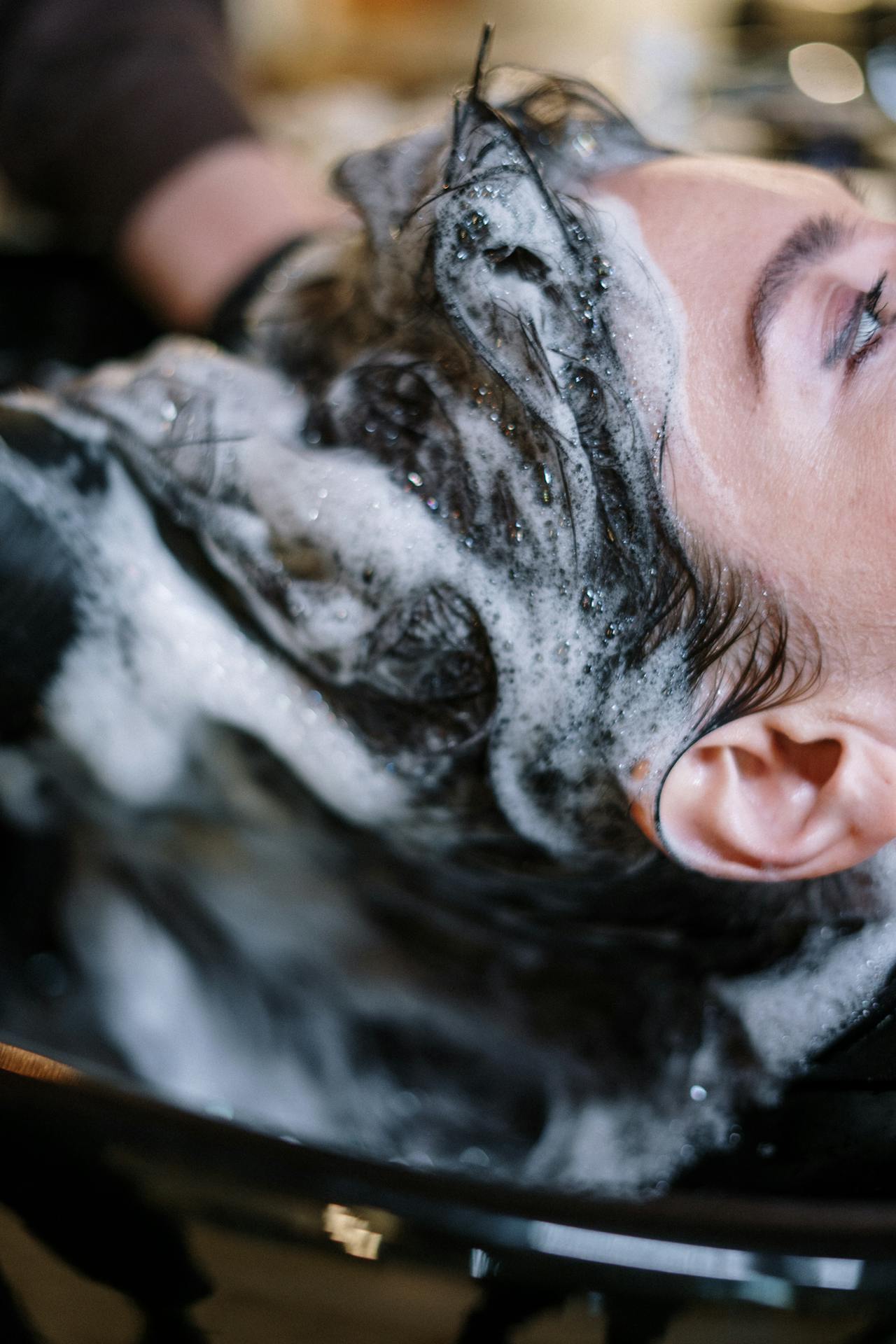 Close-up of a woman getting her hair washed at a salon, covered in shampoo foam.