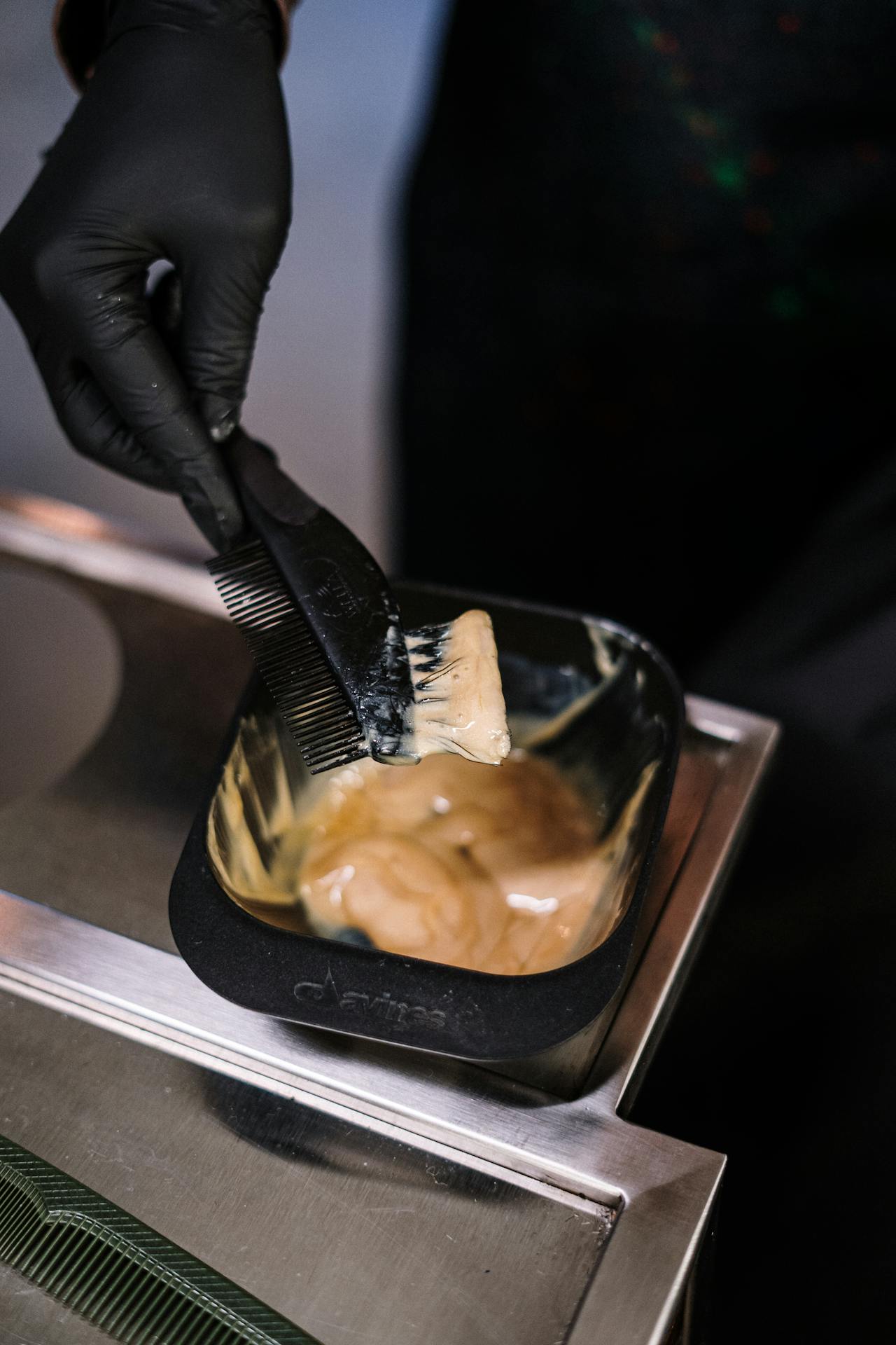 Close-up of stylist mixing hair dye with black brush in salon environment.