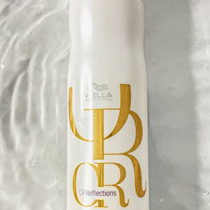 A vertical shot of a Wella shampoo bottle on a white textured surface, elegant and minimalist.