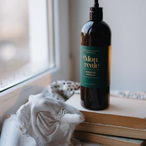 Elegant dark bottle on books by a window, exuding cozy, artistic vibes.