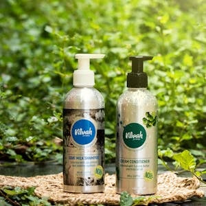 Vilvah brand eco-friendly goat milk shampoo and cream conditioner bottles displayed in a natural setting.